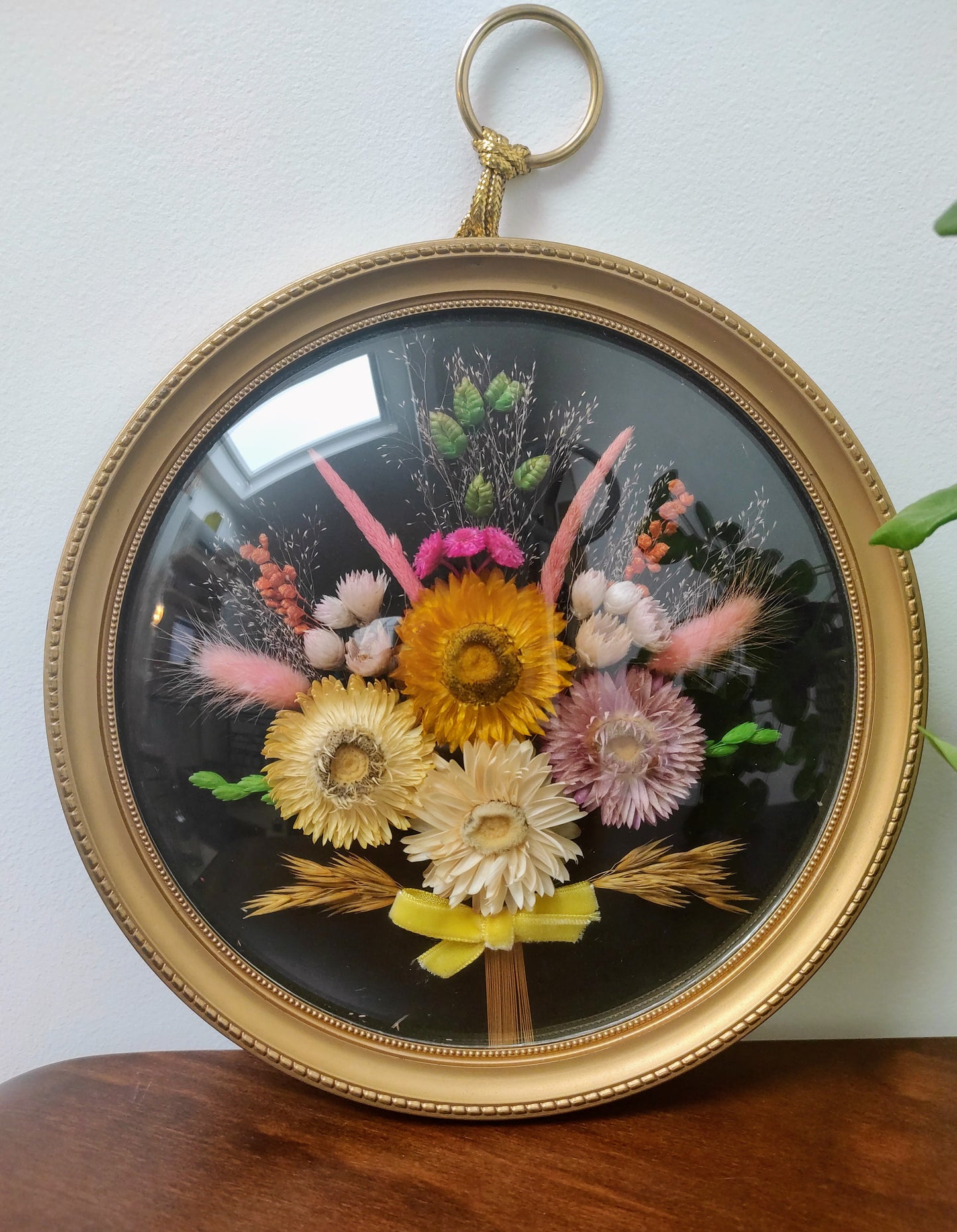 Beau cadre vintage de forme ronde avec fleurs naturelles séchées en bouquet. Le verre est bordé d’un cadre doré. Une attache est présente au dos. De belles couleurs automnales et beaucoup de charme pour ce beau cadre.
