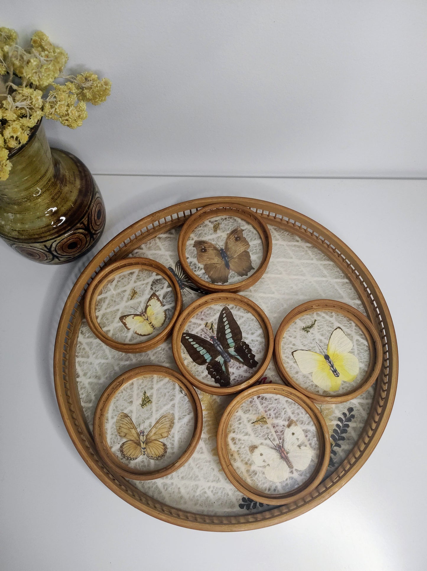 Un apéritif de prévu… Faites voyager vos convives avec ce set apéritif en rotin des années 70 composé de 6 dessous de verres papillons et leur plateau. Les sous-verres ainsi que le plateau sont en bois et composés de véritables ailes de différents papillons (corps en papier). En très bon état. Service vintage