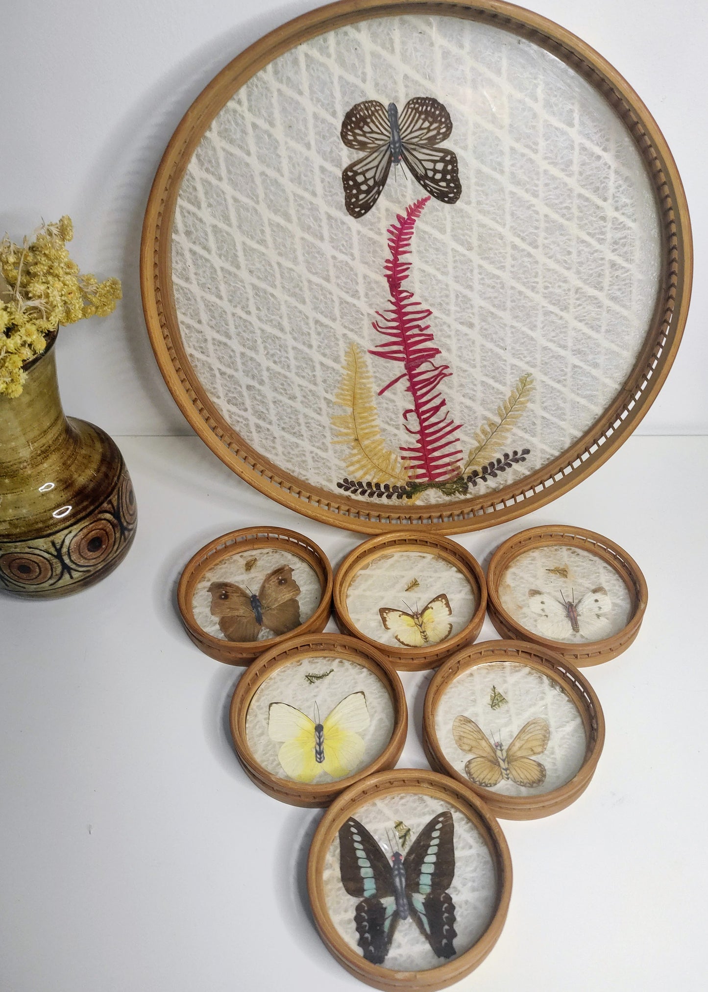 Un apéritif de prévu… Faites voyager vos convives avec ce set apéritif en rotin des années 70 composé de 6 dessous de verres papillons et leur plateau. Les sous-verres ainsi que le plateau sont en bois et composés de véritables ailes de différents papillons (corps en papier). En très bon état. Service vintage