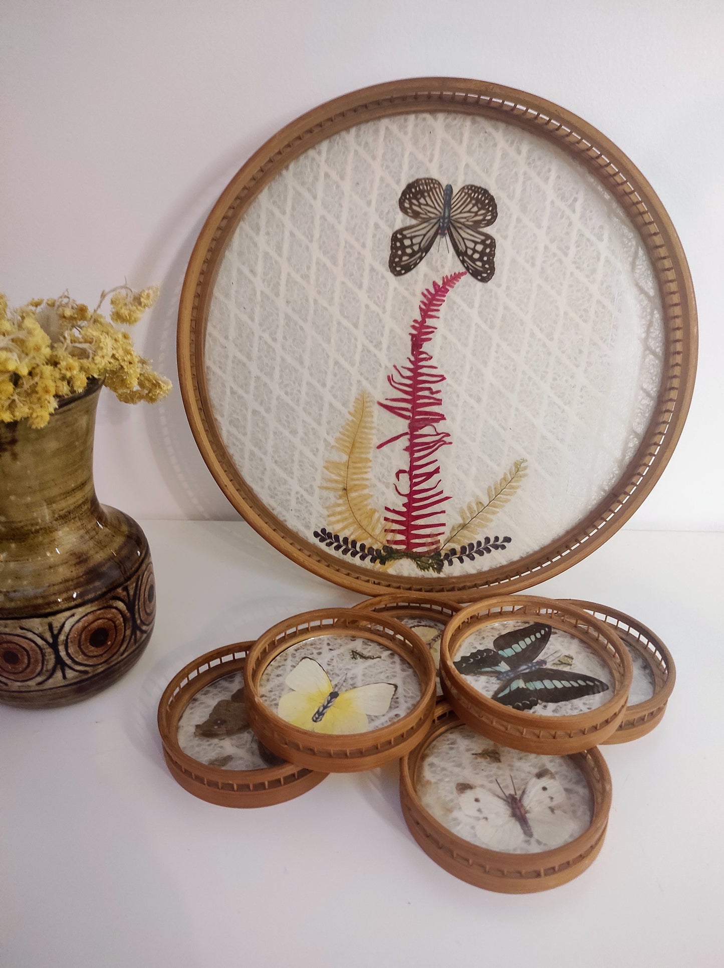 Un apéritif de prévu… Faites voyager vos convives avec ce set apéritif en rotin des années 70 composé de 6 dessous de verres papillons et leur plateau. Les sous-verres ainsi que le plateau sont en bois et composés de véritables ailes de différents papillons (corps en papier). En très bon état. Service vintage