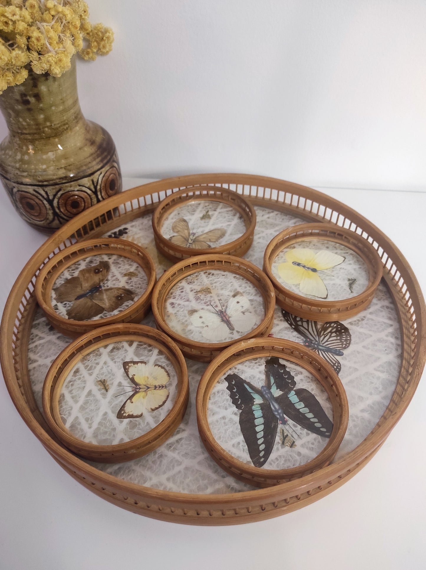 Un apéritif de prévu… Faites voyager vos convives avec ce set apéritif en rotin des années 70 composé de 6 dessous de verres papillons et leur plateau. Les sous-verres ainsi que le plateau sont en bois et composés de véritables ailes de différents papillons (corps en papier). En très bon état. Service vintage