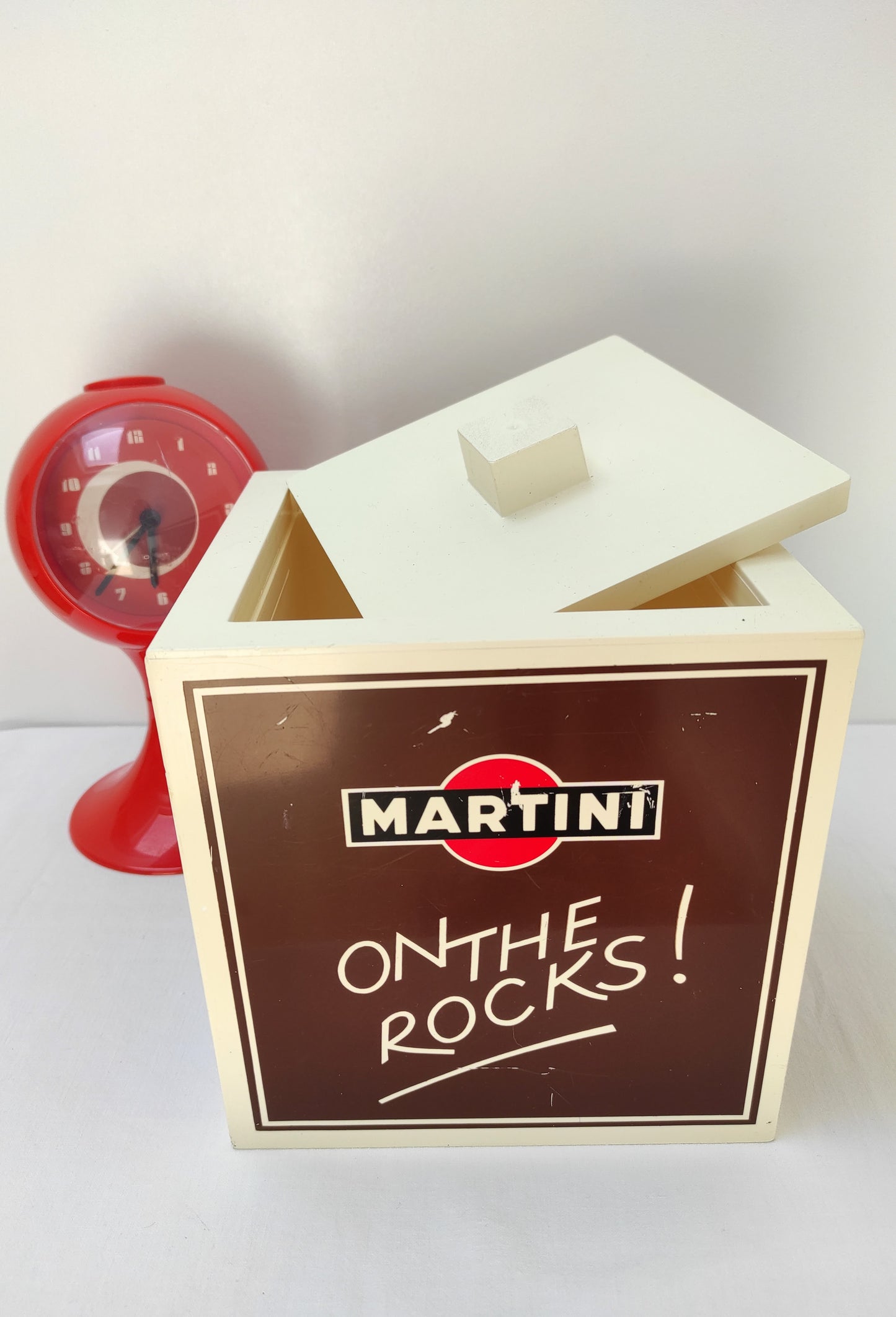 Sceau à glace en forme de cube Martini "On The Rocks". Sceau à glace ou à glaçons publicitaire Martini vintage en forme de cube en plastique de couleur marron et beige datant des années 80. Modèle assez rare, made in Italie. Sérigraphie sur les 4 faces "On The Rocks". Vos glaçons seront bien conservés grâce au couvercle.
