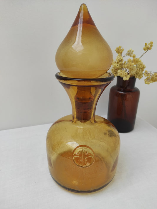 Carafe en verre ambré vintage. En décoration ou sur votre table, avec sa fleur de lys cette carafe en verre ambré ne passera pas inaperçue. Son joli gros bouchon en forme de goutte d'eau est garni de liège et plastique, quelques petites bulles dans le verre. Contenance 1L