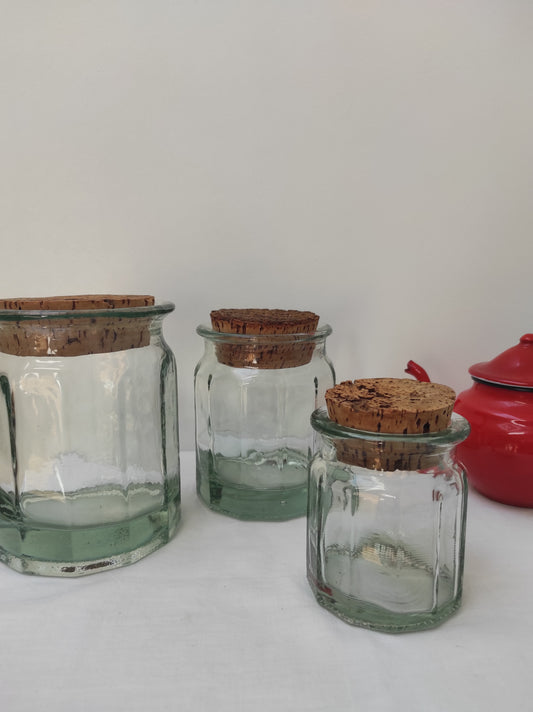 Bocal en verre vintage de 12 cm. Ancien pot en verre épais transparent aux côtés octogonaux et bouchon liège. Irrégularité et bulles dans le verre qui font tout son charme. En déco, il saura aussi faire son effet en accumulation avec d’autres formats ou couleurs. En très bon état, aucun éclat.