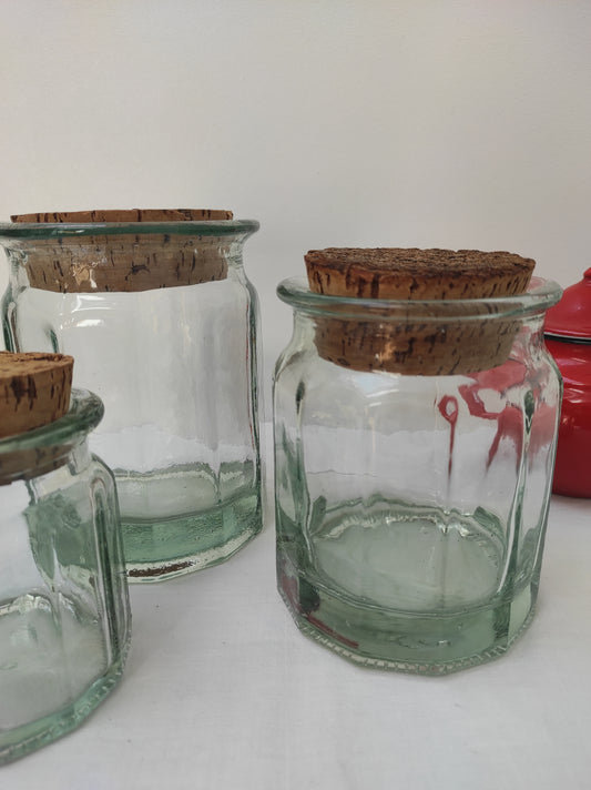 Bocal en verre vintage de 15 cm. Ancien pot en verre épais transparent aux côtés octogonaux et bouchon liège. Irrégularité et bulles dans le verre qui font tout son charme. En déco, il saura aussi faire son effet en accumulation avec d’autres formats ou couleurs. En très bon état, aucun éclat.