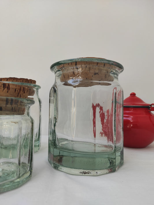 Bocal en verre vintage de 16 cm. Ancien pot en verre épais transparent aux côtés octogonaux et bouchon liège. Irrégularité et bulles dans le verre qui font tout son charme. En déco, il saura aussi faire son effet en accumulation avec d’autres formats ou couleurs. En très bon état, aucun éclat.