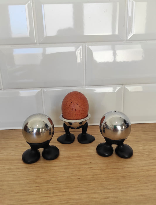 Salière, poivrière et coquetier SKS des années 70. Total look seventies pour cet ancien set composé d'une salière, une poivrière et un coquetier datant de la marque SKS. Les boules sont en inox et les pieds en plastique noirs.