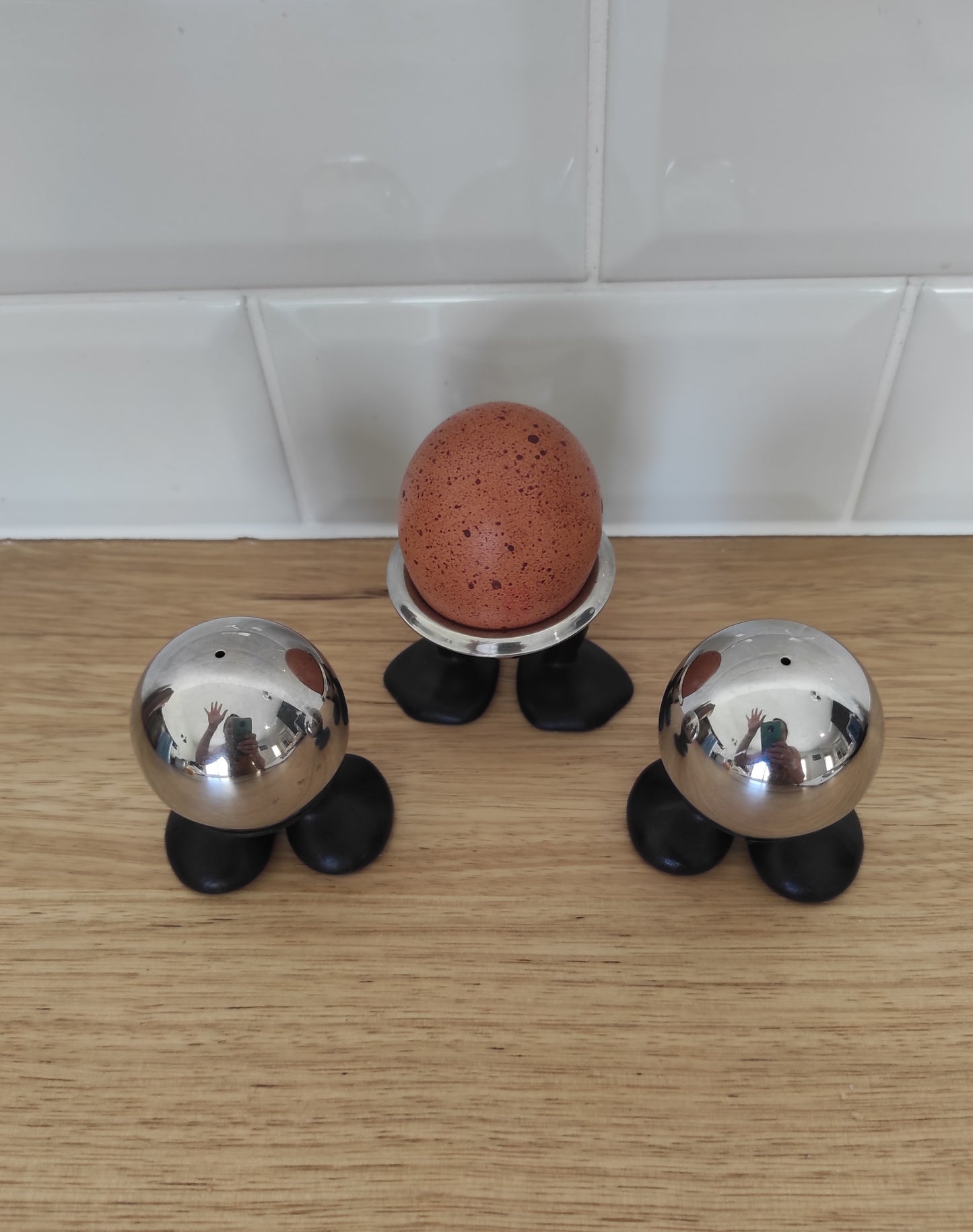 Salière, poivrière et coquetier SKS des années 70. Total look seventies pour cet ancien set composé d'une salière, une poivrière et un coquetier datant de la marque SKS. Les boules sont en inox et les pieds en plastique noirs.