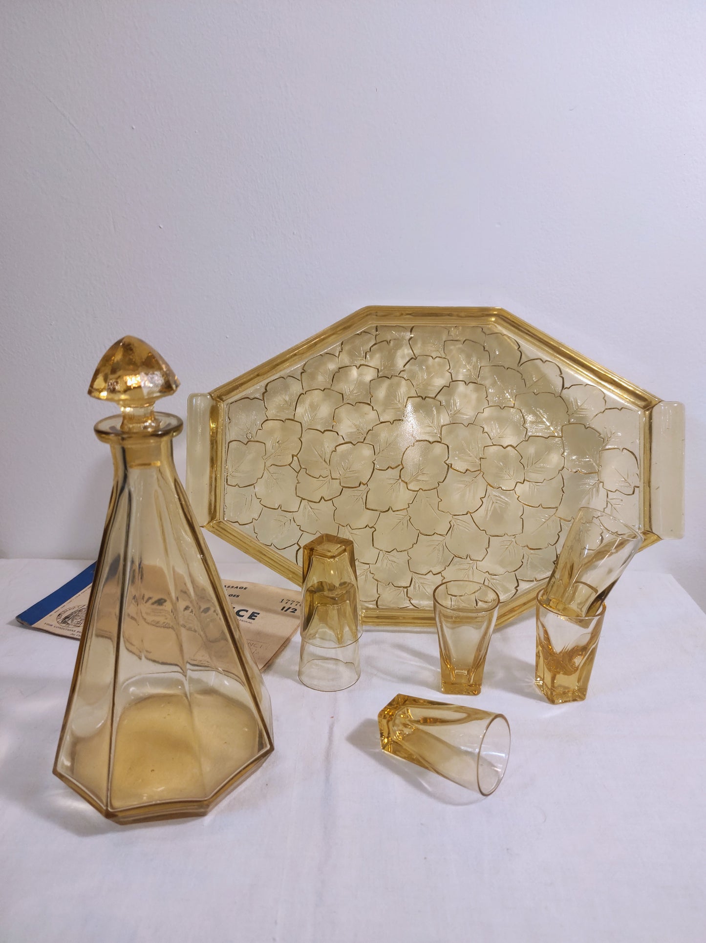 Ancien service à liqueur art déco jaune année 50. Ancien service à liqueur art déco en verre jaune comprenant 6 verres, une carafe et un plateau assez lourd aux motifs feuilles de vigne. Le service est en très bon état.