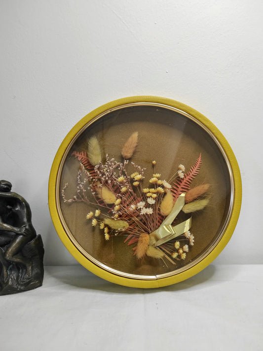 Cadre de fleurs naturelles séchées vintage. Beau Cadre vintage de forme ronde avec fleurs naturelles séchées en bouquet. Le verre est bordé d’un liseré doré. Le contour est de couleur jaune moutarde épais style simili cuir. Une attache est présente au dos. De belles couleurs automnales et beaucoup de charme pour ce beau cadre. cadre vintage