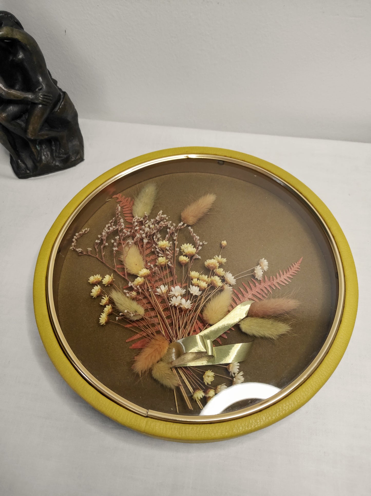 Cadre de fleurs naturelles séchées vintage. Beau Cadre vintage de forme ronde avec fleurs naturelles séchées en bouquet. Le verre est bordé d’un liseré doré. Le contour est de couleur jaune moutarde épais style simili cuir. Une attache est présente au dos. De belles couleurs automnales et beaucoup de charme pour ce beau cadre. Cadre vintage