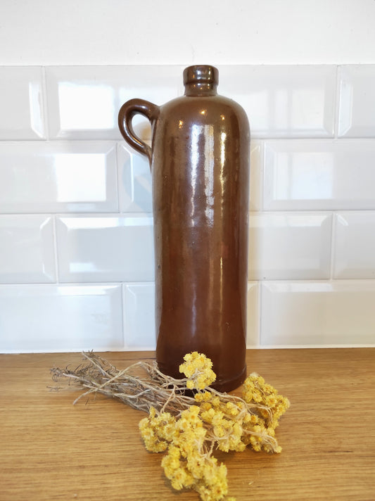 Ancienne bouteille en grès vernissé. Jolie bouteille ancienne en grès vernissé avec anse. Sa forme élancée est très décorative et accueillera à merveille vos fleurs séchées. En déco, elle fera aussi faire son effet en accumulation avec d’autres formats ou d'autres couleurs. A noter : la bouteille ayant était faite artisanalement, elle porte quelques petits défauts qui n'enlèvent rien à son charme. Aucun éclat.