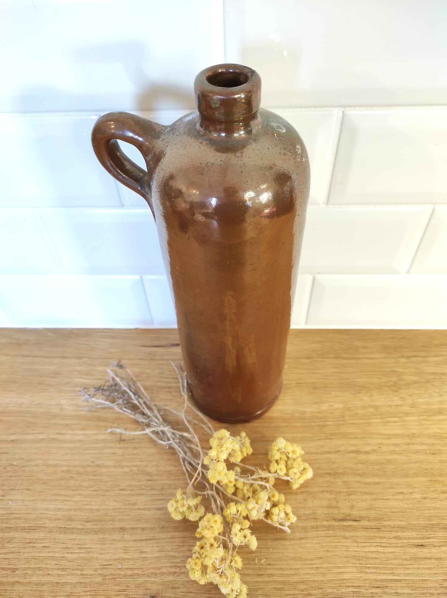 Ancienne bouteille en grès vernissé. Jolie bouteille ancienne en grès vernissé avec anse. Sa forme élancée est très décorative et accueillera à merveille vos fleurs séchées. En déco, elle fera aussi faire son effet en accumulation avec d’autres formats ou d'autres couleurs. A noter : la bouteille ayant était faite artisanalement, elle porte quelques petits défauts qui n'enlèvent rien à son charme. Aucun éclat.