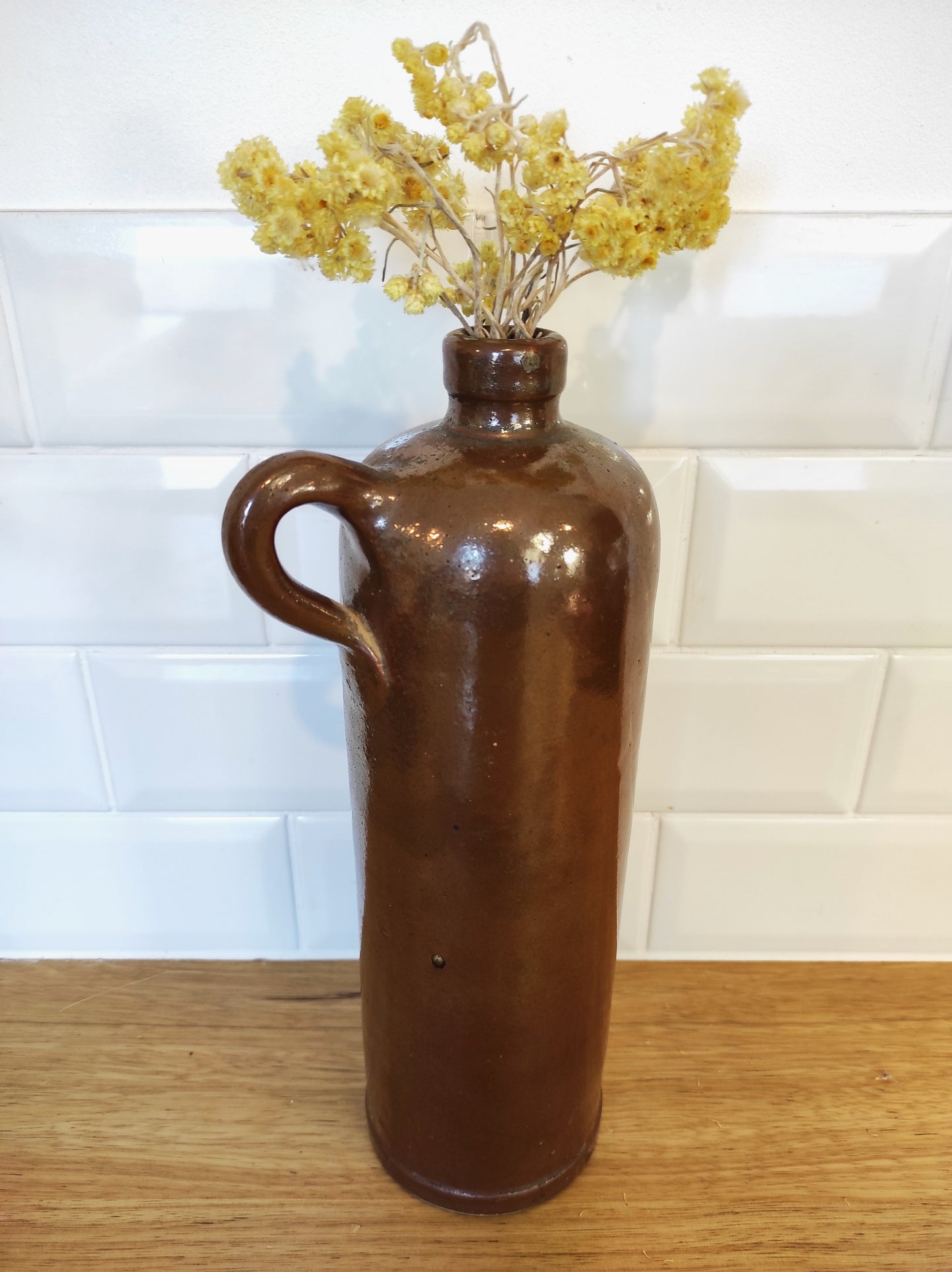 Ancienne bouteille en grès vernissé. Jolie bouteille ancienne en grès vernissé avec anse. Sa forme élancée est très décorative et accueillera à merveille vos fleurs séchées. En déco, elle fera aussi faire son effet en accumulation avec d’autres formats ou d'autres couleurs. A noter : la bouteille ayant était faite artisanalement, elle porte quelques petits défauts qui n'enlèvent rien à son charme. Aucun éclat.