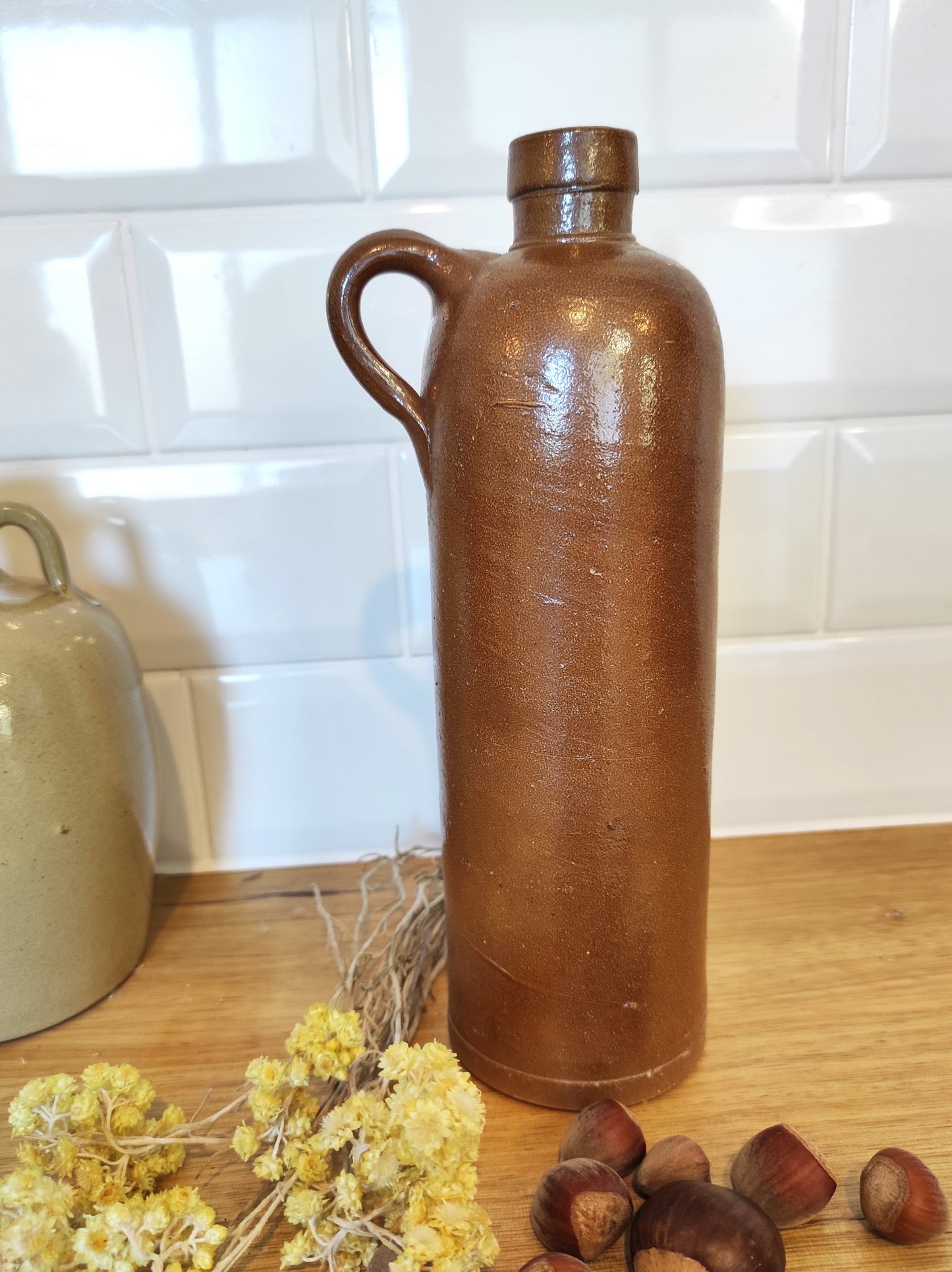 Ancienne bouteille en grès vernissé 23 cm. Jolie bouteille ancienne en grès vernissé avec anse. Un peu plus petite que sa grande sœur elle reste tout de même très décorative et accueillera à merveille vos fleurs séchées. En déco, elle fera aussi faire son effet en accumulation avec d’autres formats ou d'autres couleurs. Bouteille vintage