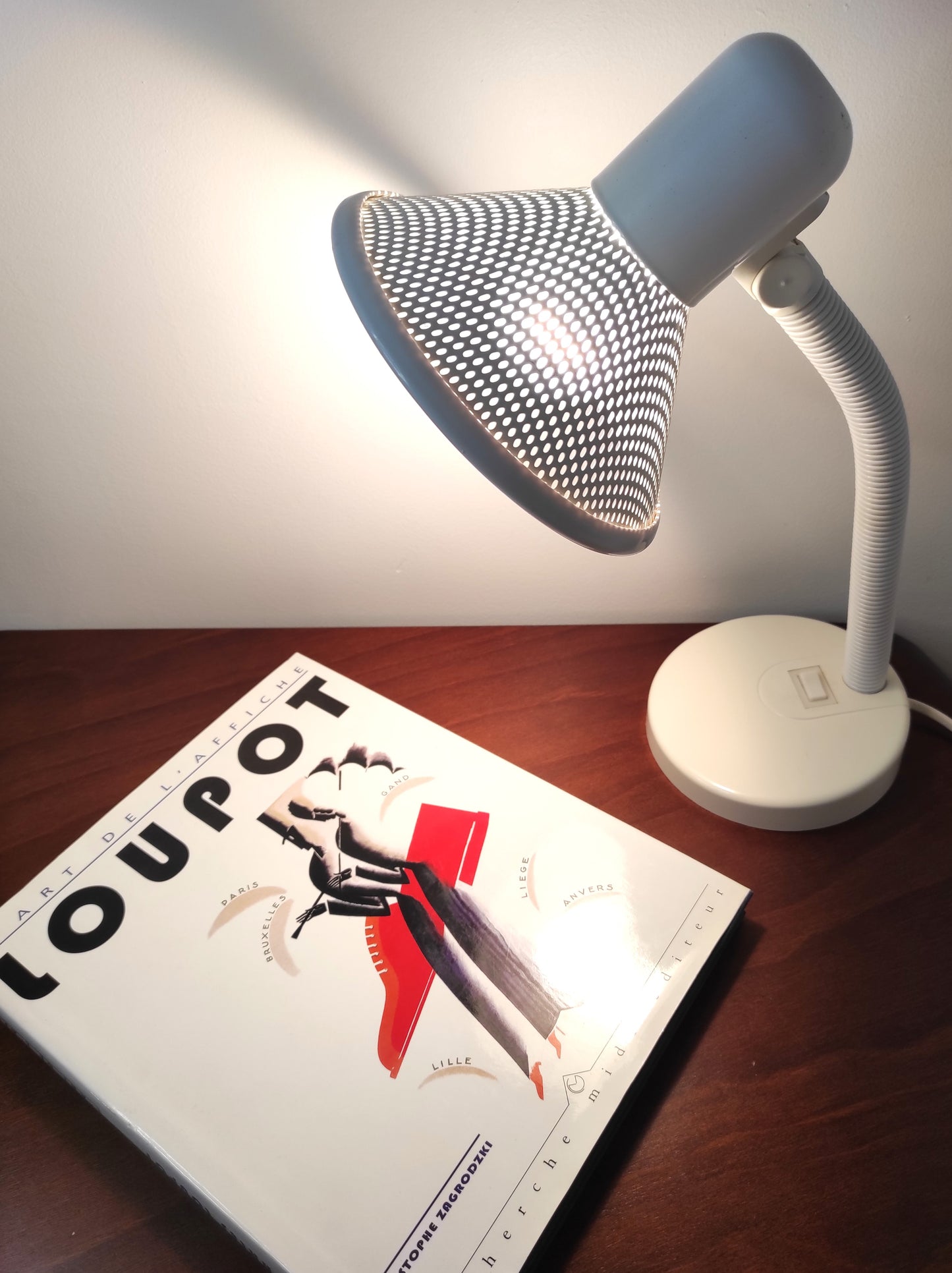 Lampe de bureau blanche des années 80. Ancienne lampe de bureau, lampe à poser en aluminium blanc des années 80 son abat-jour ajouré est orientable (haut/bas) et son interrupteur est sur le pied. Electrification d'origine vérifiée, en bon état, ampoule vis.