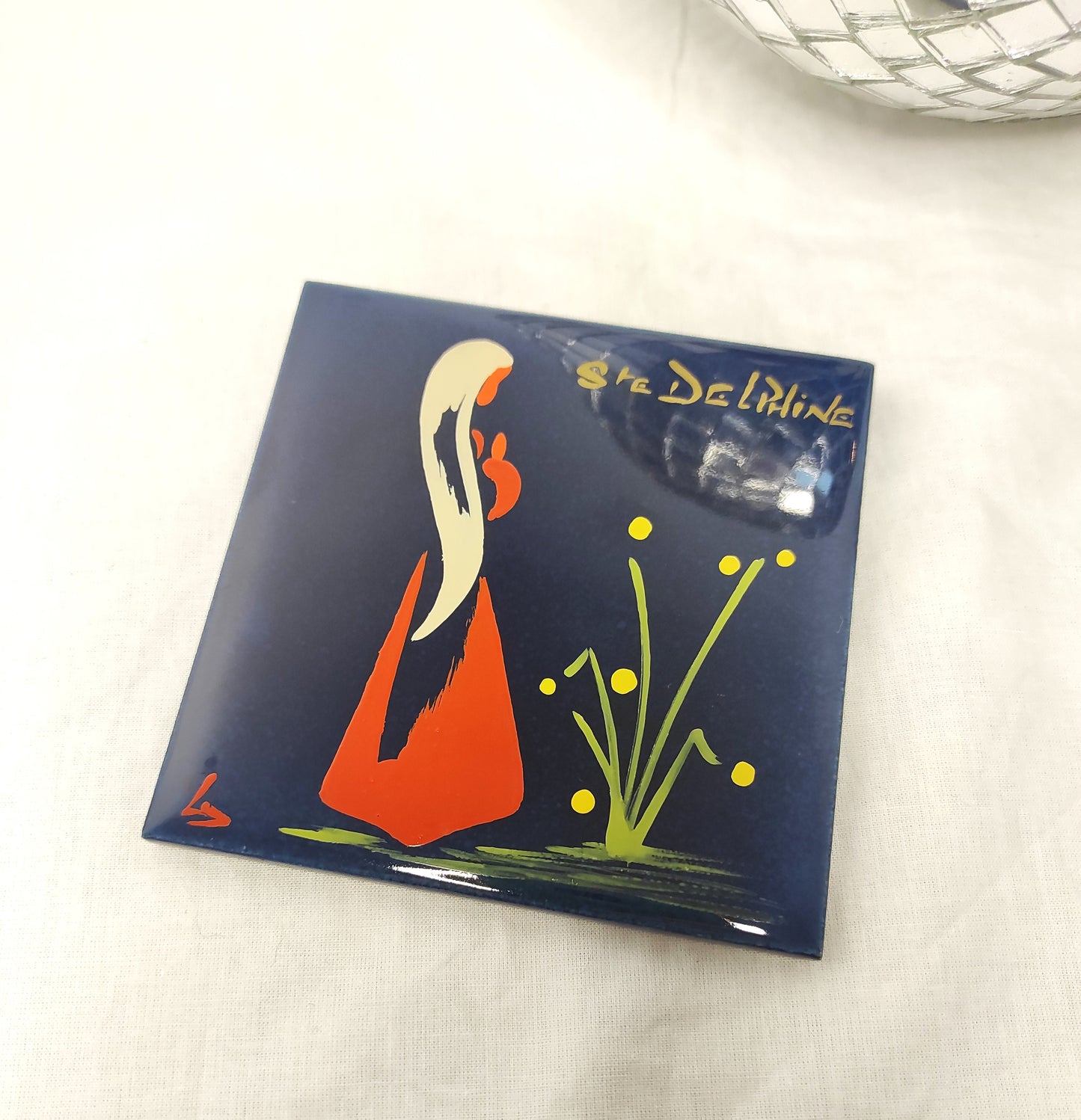 Ancien carreau en céramique religieux peint à la main. Cet ancien carreau religieux en céramique e couleur bleu nuit peint à la main représentant Ste Delphine trouvera sa place dans votre intérieur....ou dans celui d'une Delphine ! Au dos de ce carreau vous trouverez la petite histoire de Ste Delphine sur une feutrine bleu turquoise. En bon état général, léger petit éclat dans coin haut gauche mais ne se voit pas une fois au mur (voir photo) . Attache à l'arrière. Décoration murale vintage.