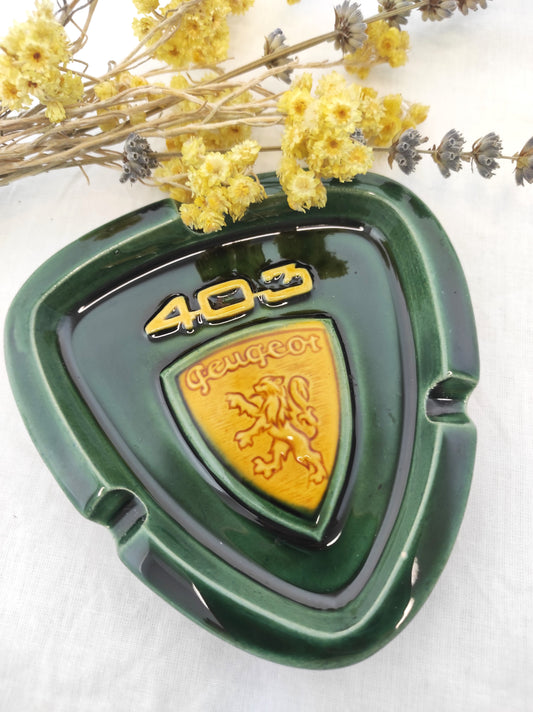 Rare cendrier publicitaire des années 60 PEUGEOT 403. RARE cendrier publicitaire des années 60 pour la Peugeot 403 en faïence de couleur vert sapin et jaune moutarde. Il fera une superbe déco rétro et colorée sur une étagère ou un joli vide poche sur une commode ! A noter : un mini éclat à peine visible (voir photo) mais en très bon état vu son âge, signé au dos. Décoration vintage.