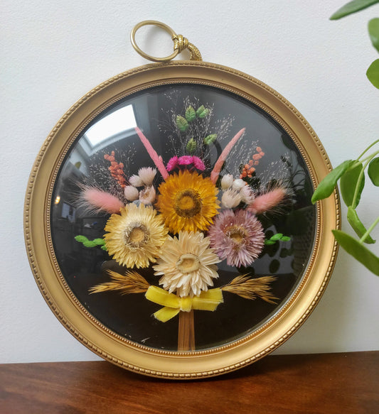 Beau cadre vintage de forme ronde avec fleurs naturelles séchées en bouquet.  Le verre est bordé d’un cadre doré.  Une attache est présente au dos.  De belles couleurs automnales et beaucoup de charme pour ce beau cadre.