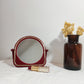 Miroir à poser en plastique rouge vintage. Ancien petit miroir à poser en plastique rouge et liseré doré des années 70/80.  A noter : des traces du temps, léger coup sur le plastique en haut du miroir (voir photo)  Dimensions : 15 cm x 15 cm  Poids : 190 gr