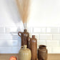 Ancienne bouteille en grès vernissé. Jolie bouteille ancienne en grès vernissé avec anse.  Sa forme élancée est très décorative et accueillera à merveille vos fleurs séchées.   En déco, elle fera aussi faire son effet en accumulation avec d’autres formats ou d'autres couleurs.  A noter : la bouteille ayant était faite artisanalement, elle porte quelques petits défauts qui n'enlèvent rien à son charme. Aucun éclat.