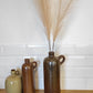 Ancienne bouteille en grès vernissé. Jolie bouteille ancienne en grès vernissé avec anse.  Sa forme élancée est très décorative et accueillera à merveille vos fleurs séchées.   En déco, elle fera aussi faire son effet en accumulation avec d’autres formats ou d'autres couleurs.  A noter : la bouteille ayant était faite artisanalement, elle porte quelques petits défauts qui n'enlèvent rien à son charme. Aucun éclat.
