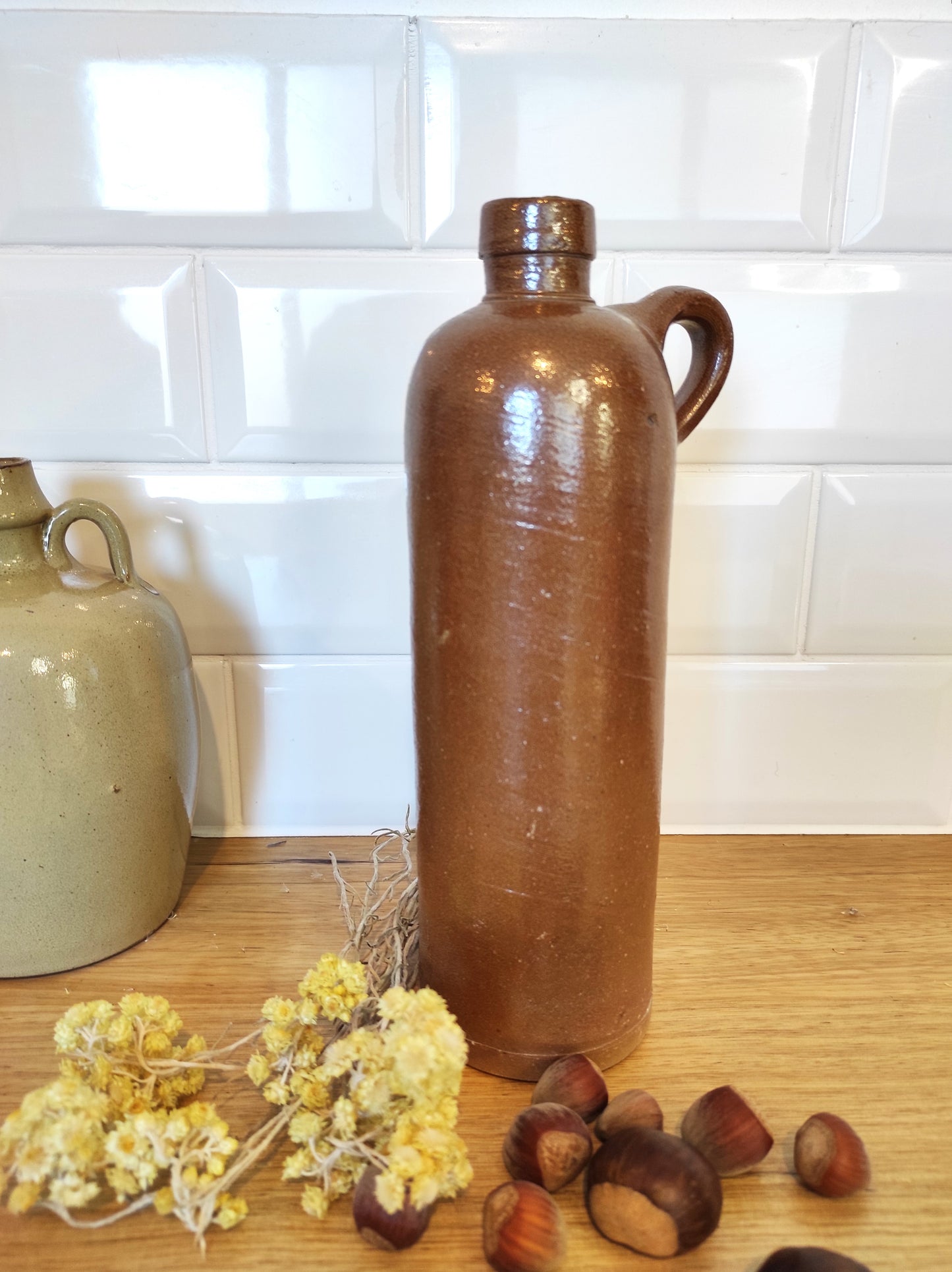 Ancienne bouteille en grès vernissé 23 cm. Jolie bouteille ancienne en grès vernissé avec anse.  Un peu plus petite que sa grande sœur elle reste tout de même très décorative et accueillera à merveille vos fleurs séchées.   En déco, elle fera aussi faire son effet en accumulation avec d’autres formats ou d'autres couleurs. Bouteille vintage